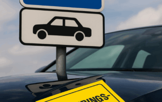 Billede af et parkeringstavle med hvidt P på blå baggrund og sort bilsymbol under, foran en mørk bil med en gul seddel på motorhjelmen med teksten “PARKERINGS-AFGIFT”.